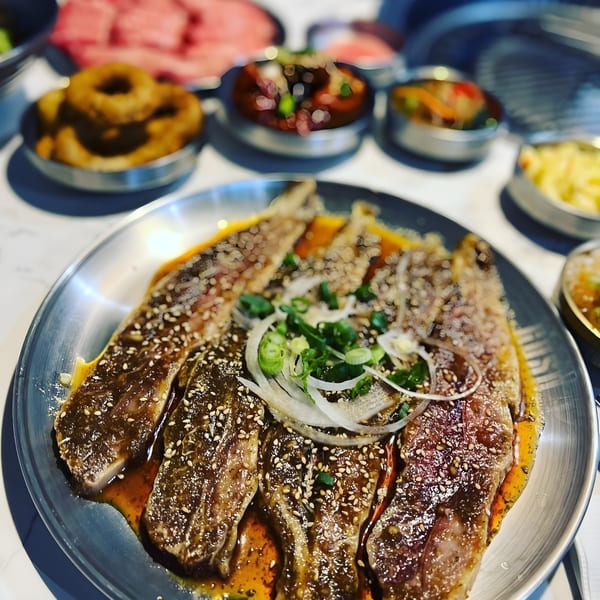 Marinated Korean BBQ short ribs with sesame seeds and green onions, surrounded by various side dishes.