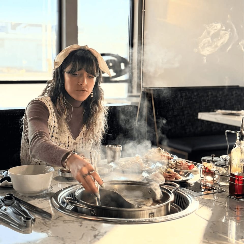 A woman cooking shabu shabu at Gosu Korean BBQ, with steam rising from the pot.