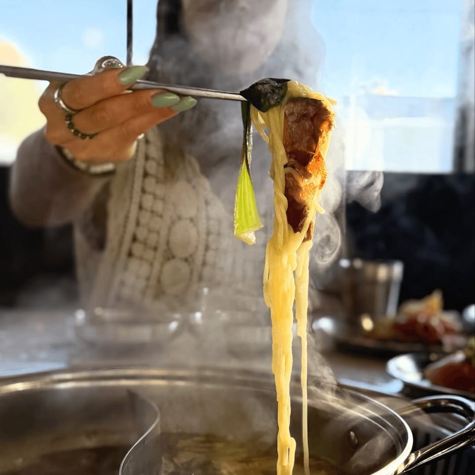 Chopsticks lifting noodles, meat, and greens from a steaming shabu shabu pot at Gosu Korean BBQ.