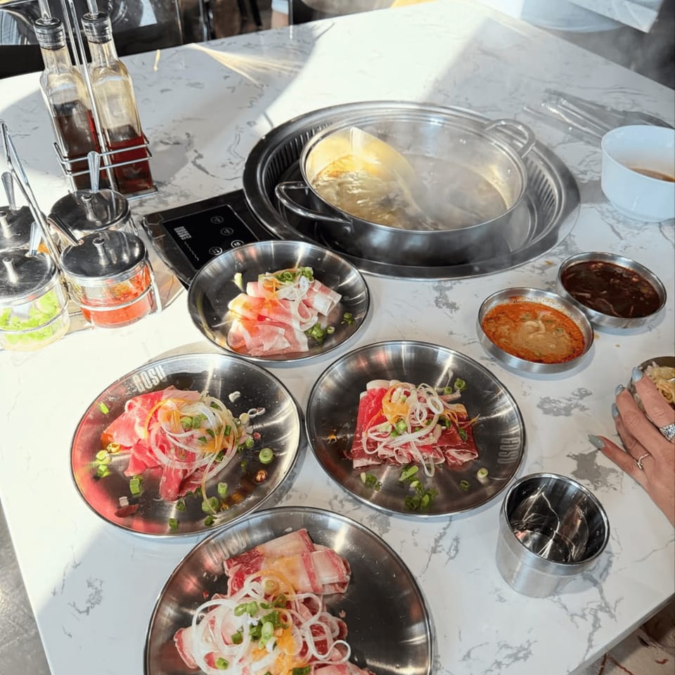Tabletop view of Gosu Korean BBQ & Shabu Shabu with hot pot, raw meats, and sauces.