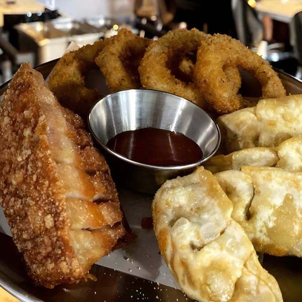 A platter of crispy fried Korean appetizers, including onion rings, dumplings, and a large fried cutlet.