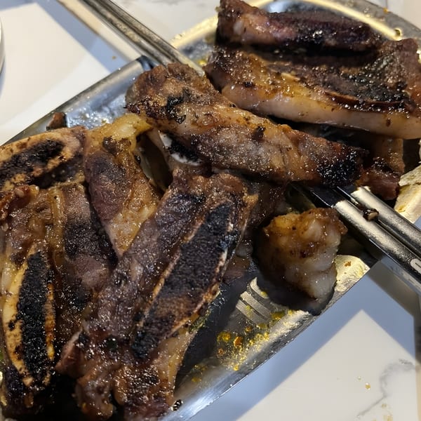 Close-up of grilled Korean BBQ short ribs on a metal tray with tongs.